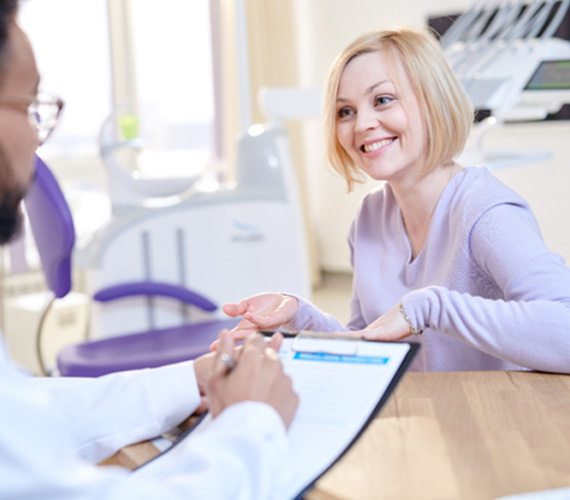 a woman smiling and speaking with her cosmetic dentist