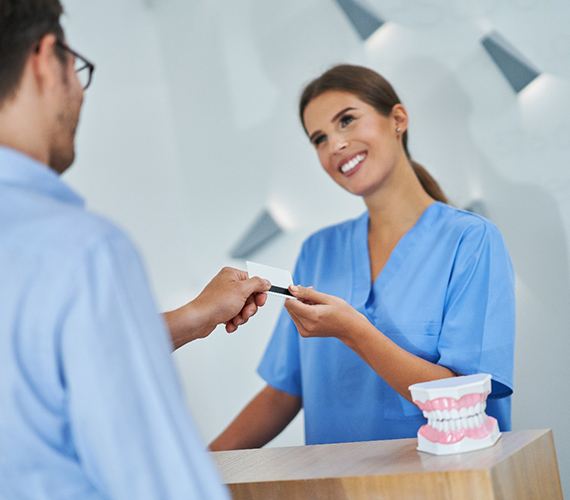 A female dental receptionist accepts the male patient’s credit card to pay for his dental exam