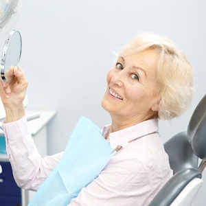 Senior dental patient using mirror to admire her restorations