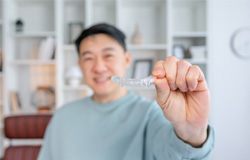 Closeup of smiling patient holding Invisalign clear aligner