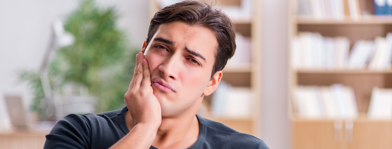 Man in need of emergency dentistry holding cheek in pain