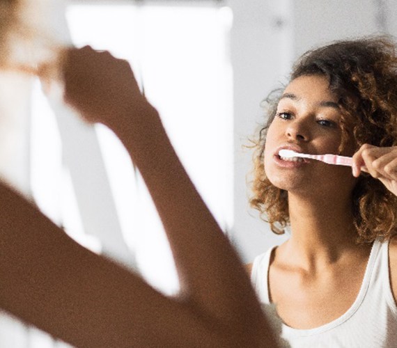 Woman in white shirt brushing her teeth in bathroom
