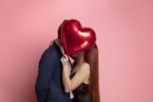 a couple kissing behind a Valentine's Day balloon