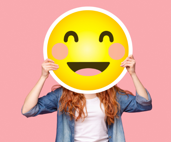 Woman holding smile emoji over her face