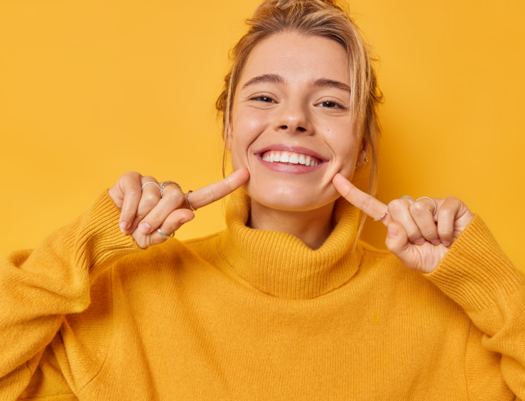 Woman in yellow turtleneck on yellow background pointing at smile
